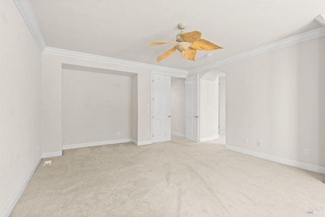 spare room featuring light carpet, ornamental molding, arched walkways, baseboards, and ceiling fan