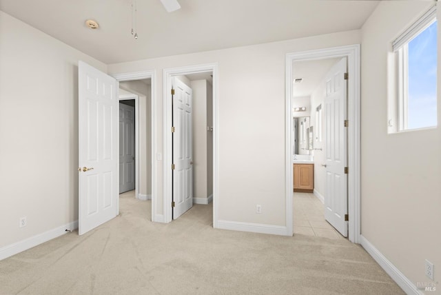 unfurnished bedroom with baseboards, light carpet, ensuite bath, and a spacious closet