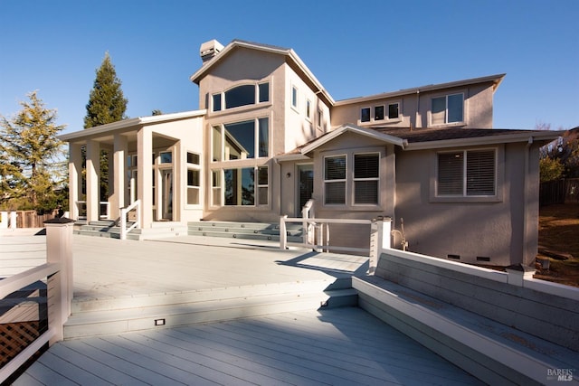 rear view of house with stucco siding, a chimney, and a deck