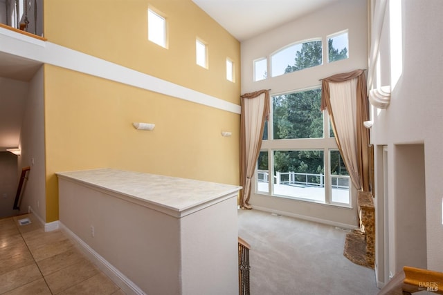 hall featuring visible vents, a high ceiling, light tile patterned floors, baseboards, and light colored carpet