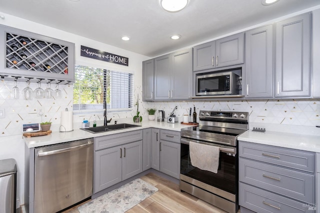 kitchen featuring stainless steel appliances, sink, light wood-type flooring, backsplash, and gray cabinets