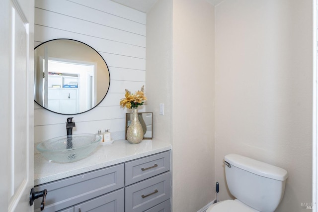 bathroom with toilet, wood walls, and vanity