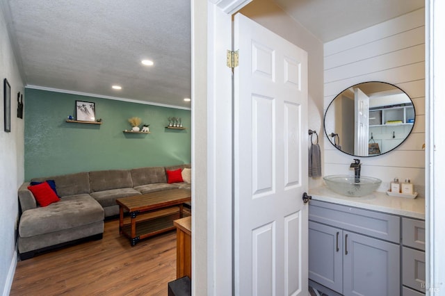 bathroom with a textured ceiling, wood walls, crown molding, wood-type flooring, and vanity