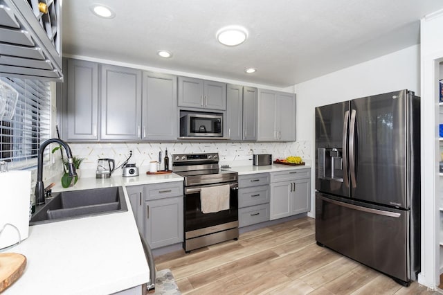 kitchen with light wood-type flooring, appliances with stainless steel finishes, gray cabinets, and sink