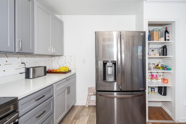 kitchen with light stone counters, tasteful backsplash, light hardwood / wood-style flooring, stainless steel fridge with ice dispenser, and gray cabinets