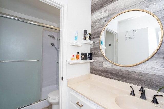 bathroom with vanity, wood walls, a shower with shower door, and toilet