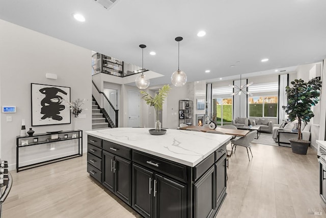 kitchen featuring light stone countertops, a center island, decorative light fixtures, a chandelier, and light hardwood / wood-style flooring