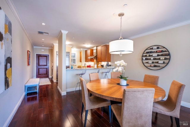 dining space featuring dark hardwood / wood-style floors, crown molding, and ornate columns