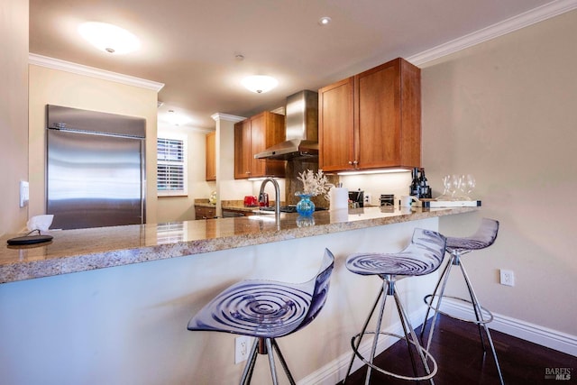 kitchen with light stone counters, stainless steel built in fridge, ornamental molding, and wall chimney exhaust hood