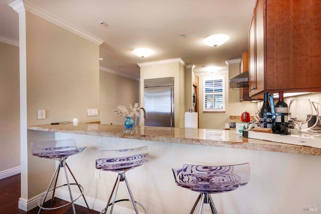 kitchen with dark wood-type flooring, built in fridge, range hood, ornamental molding, and light stone counters