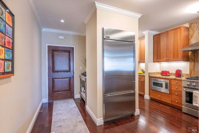 kitchen with dark wood-type flooring, wall chimney exhaust hood, crown molding, and built in appliances