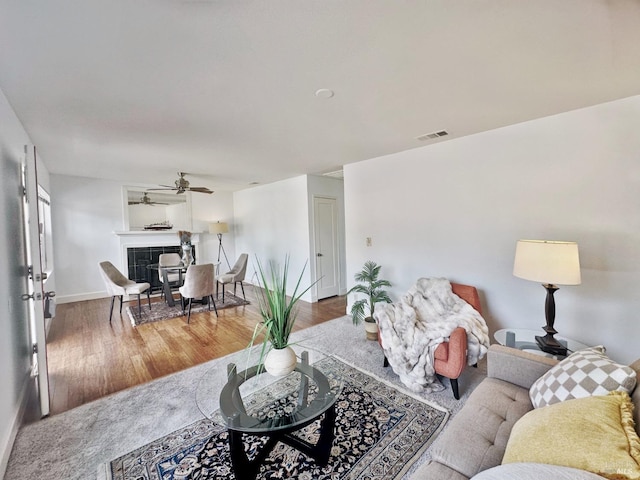 living room with ceiling fan, a tiled fireplace, and hardwood / wood-style flooring