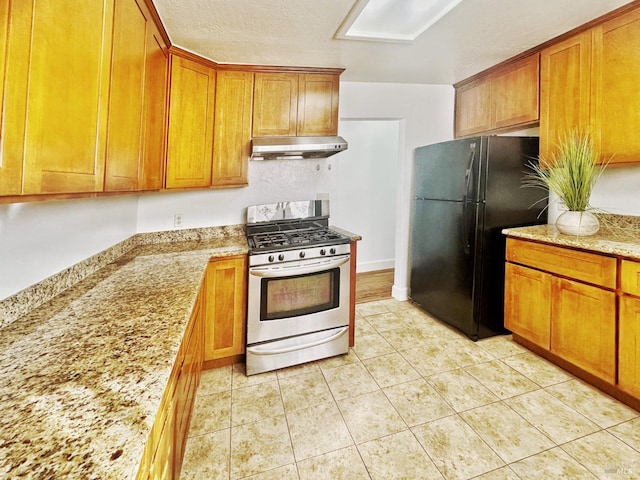 kitchen featuring black fridge, stainless steel range with gas stovetop, light stone countertops, a textured ceiling, and light tile patterned floors