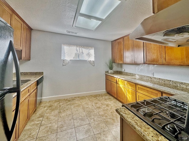 kitchen featuring light tile patterned floors, dishwasher, range hood, and black fridge