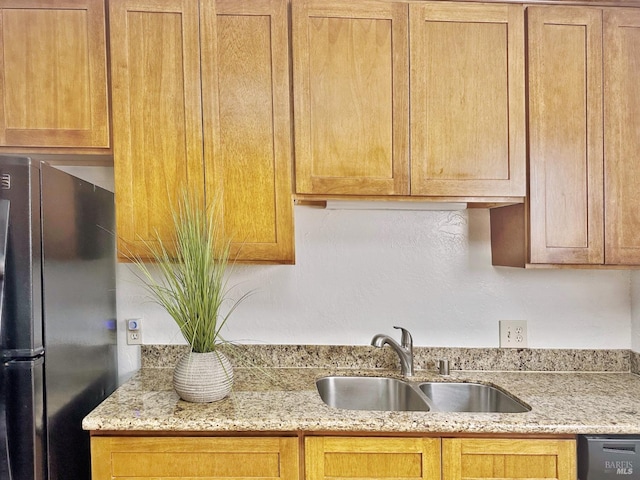 kitchen featuring light stone countertops, stainless steel fridge, and sink