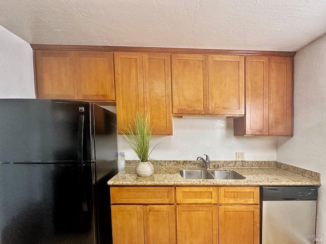 kitchen featuring black fridge, a textured ceiling, stainless steel dishwasher, light stone counters, and sink