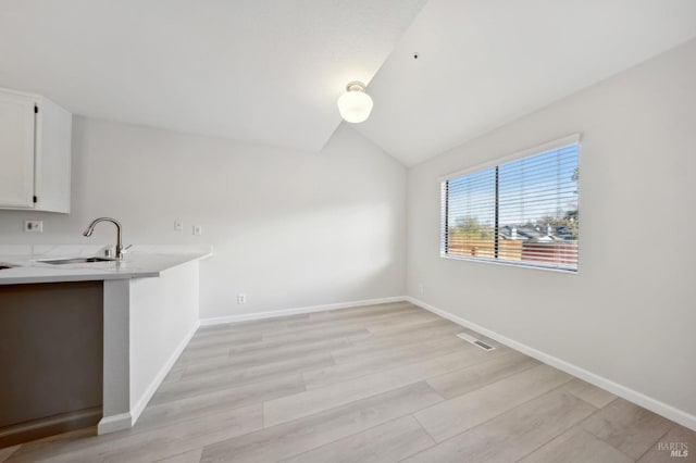 interior space featuring sink, light hardwood / wood-style flooring, white cabinetry, and lofted ceiling