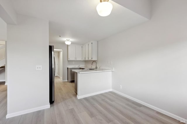 kitchen with sink, white cabinetry, light hardwood / wood-style floors, kitchen peninsula, and stainless steel refrigerator