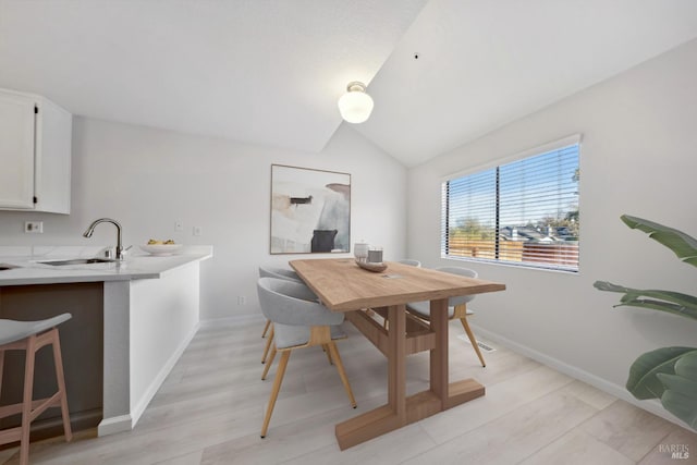 dining area with sink, light hardwood / wood-style floors, and vaulted ceiling