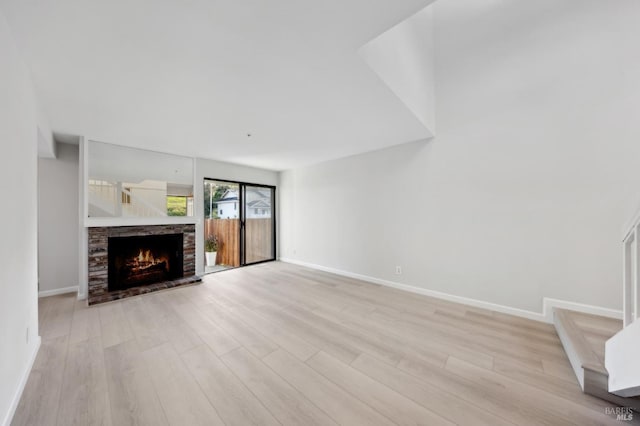 unfurnished living room with light hardwood / wood-style flooring and a stone fireplace