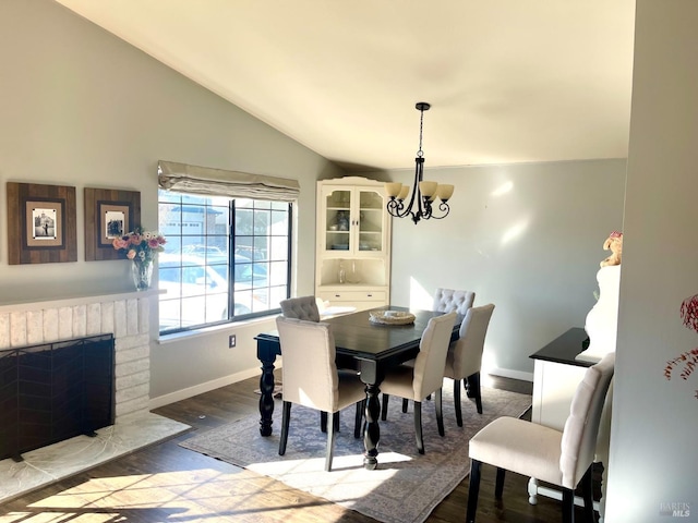 dining space with lofted ceiling, a fireplace, light wood-type flooring, and a notable chandelier