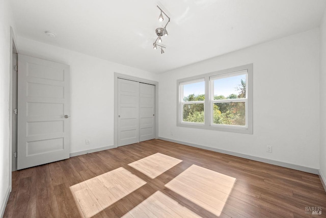 unfurnished bedroom featuring hardwood / wood-style flooring, rail lighting, and a closet