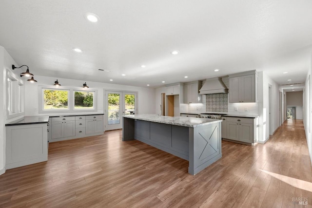 kitchen featuring light hardwood / wood-style flooring, custom range hood, decorative backsplash, a large island, and gray cabinets