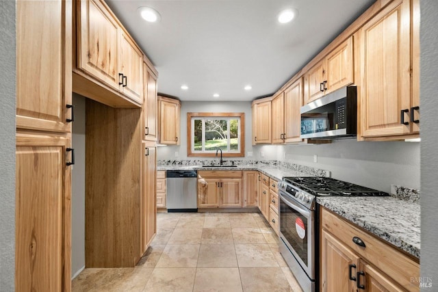 kitchen featuring light stone counters, stainless steel appliances, light brown cabinetry, light tile patterned floors, and sink