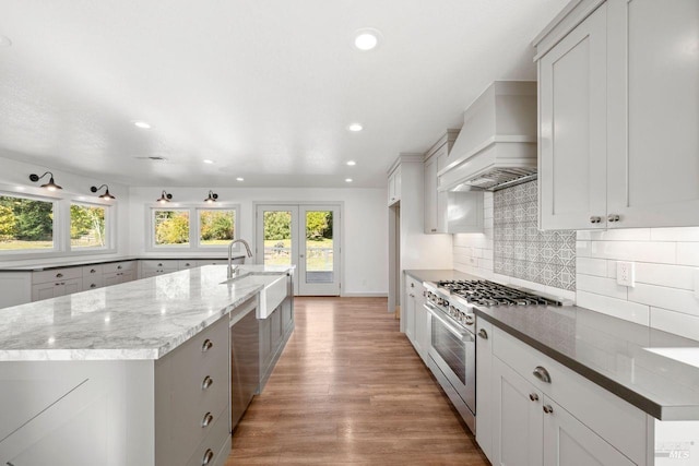 kitchen with light stone counters, stainless steel appliances, custom range hood, a large island, and backsplash