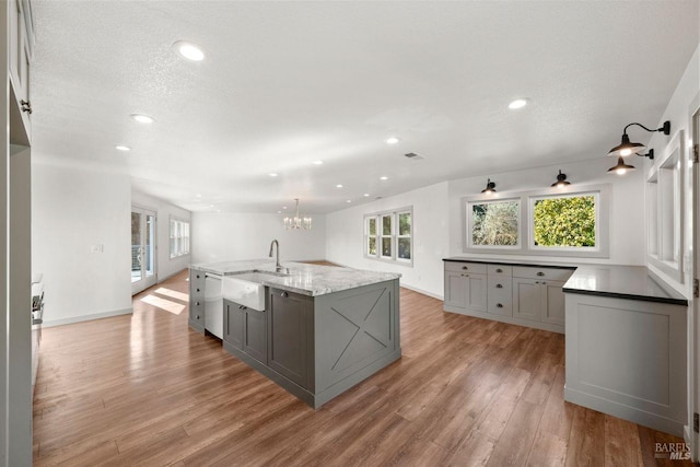 kitchen featuring gray cabinetry, light hardwood / wood-style floors, a large island with sink, a notable chandelier, and a wealth of natural light