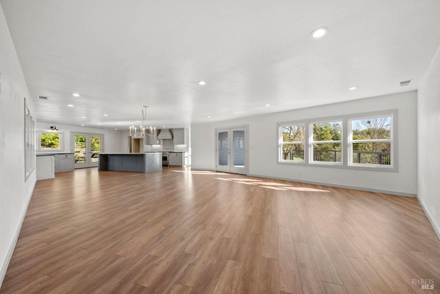 unfurnished living room with an inviting chandelier and light wood-type flooring