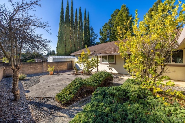 view of front of house featuring a patio area, a fenced backyard, a tile roof, and stucco siding