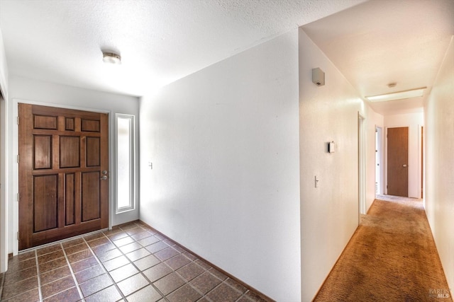 foyer featuring a textured ceiling, dark colored carpet, and dark tile patterned flooring