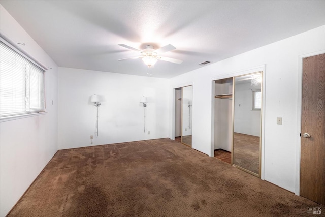 unfurnished bedroom with a ceiling fan, visible vents, dark carpet, and two closets