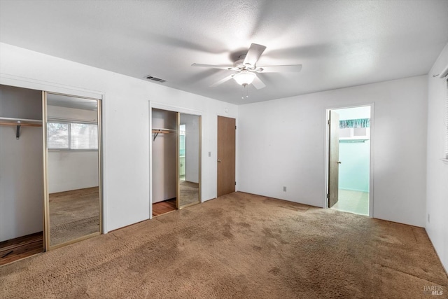 unfurnished bedroom featuring two closets, visible vents, carpet flooring, ceiling fan, and ensuite bath