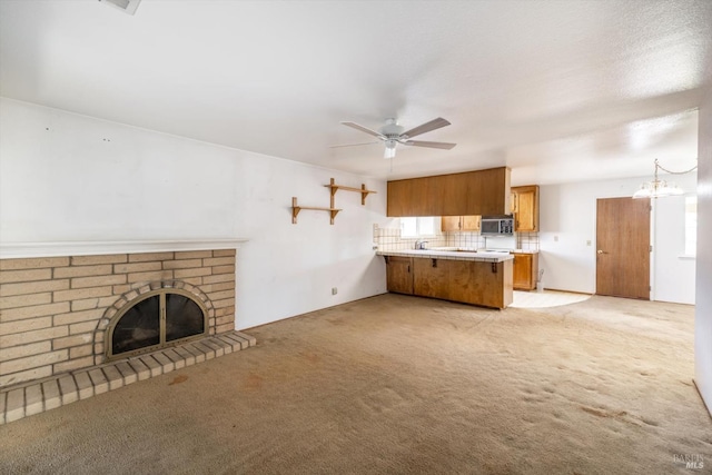 unfurnished living room featuring a fireplace, ceiling fan with notable chandelier, and light colored carpet