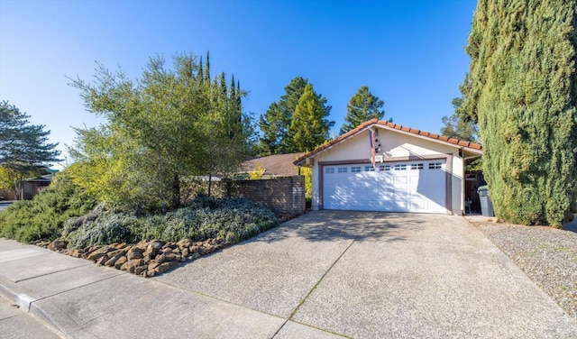 ranch-style house featuring an attached garage, a tiled roof, concrete driveway, and stucco siding