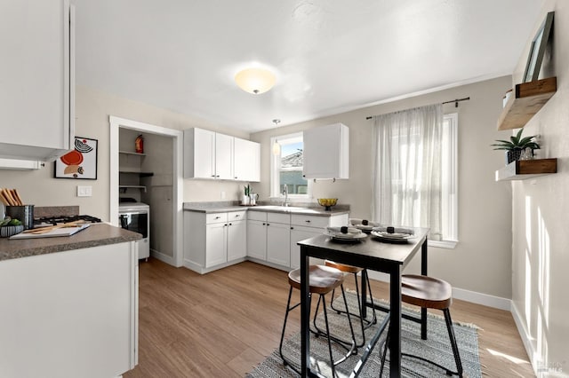 kitchen with sink, white cabinets, stove, and light hardwood / wood-style flooring