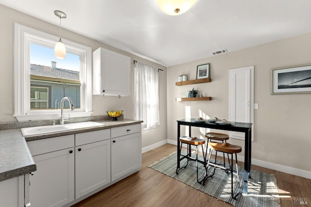 kitchen featuring sink, light hardwood / wood-style floors, hanging light fixtures, and white cabinetry