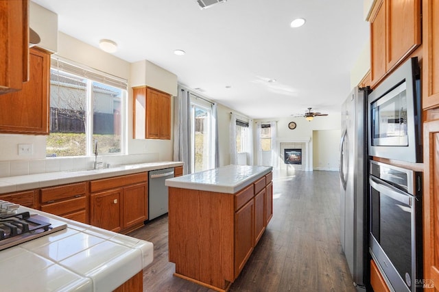 kitchen featuring ceiling fan, stainless steel appliances, tile counters, a center island, and sink