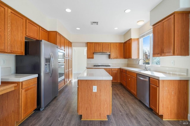 kitchen featuring dark wood-type flooring, appliances with stainless steel finishes, sink, and a center island