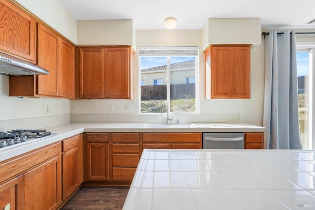 kitchen featuring tile countertops, gas cooktop, dark wood-type flooring, dishwasher, and sink