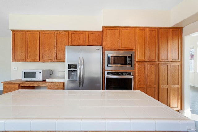 kitchen with appliances with stainless steel finishes, tile countertops, and a kitchen island