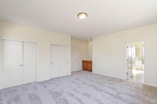 unfurnished bedroom featuring light carpet and two closets