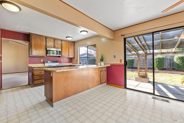 kitchen with a peninsula, light countertops, brown cabinets, stainless steel microwave, and white electric range oven