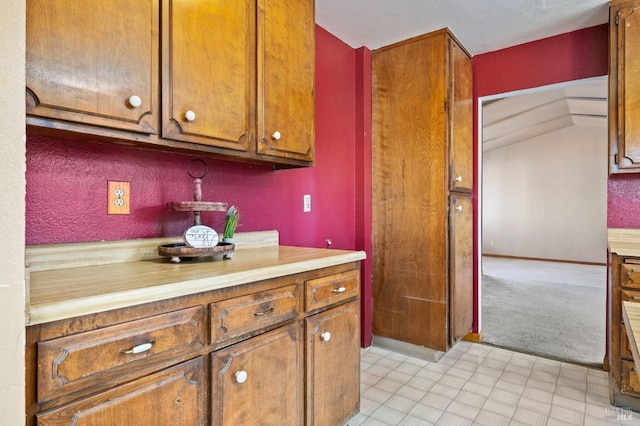 kitchen featuring light countertops, brown cabinetry, light colored carpet, and baseboards