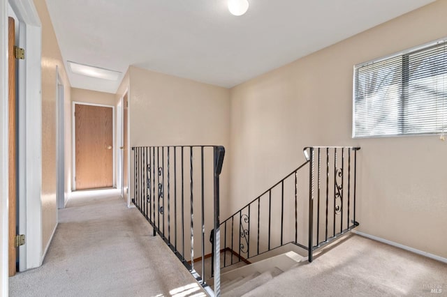 hallway featuring baseboards, attic access, an upstairs landing, and light colored carpet