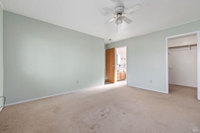 unfurnished bedroom featuring light carpet, a spacious closet, ensuite bathroom, and baseboards