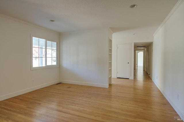 spare room with built in shelves, crown molding, and light wood-type flooring