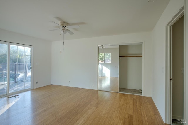 unfurnished bedroom featuring ceiling fan, access to outside, multiple windows, light wood-type flooring, and a closet